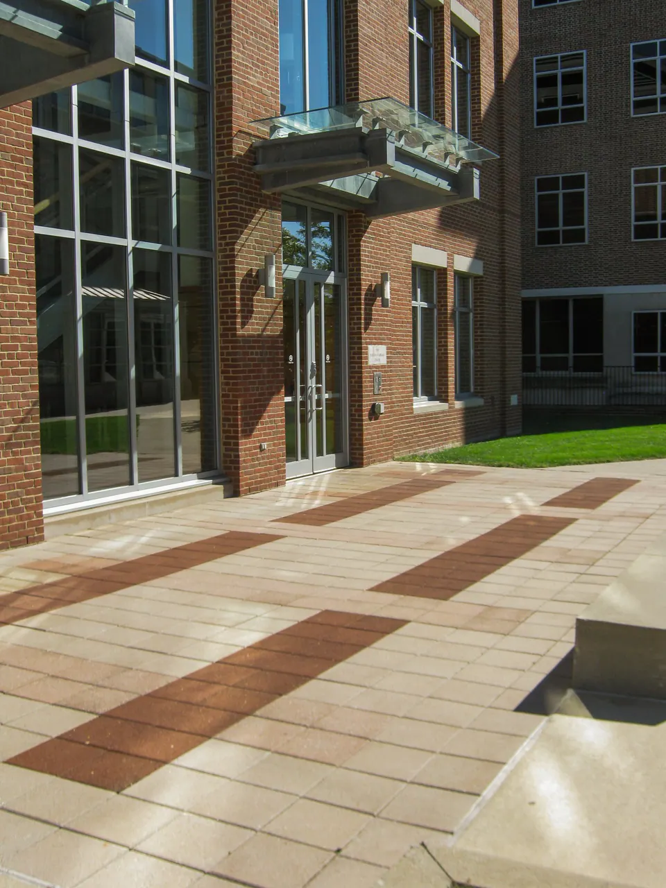 Campus entry paving with concrete fields, brick bands, glass building entry, and lawn edge